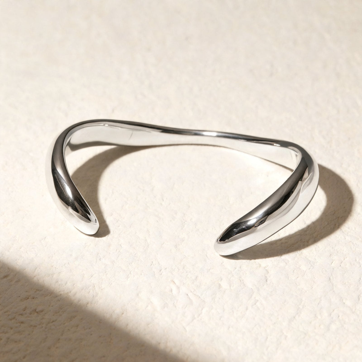 The Twist Cuff in silver, open sculptural cuff on ivory plaster