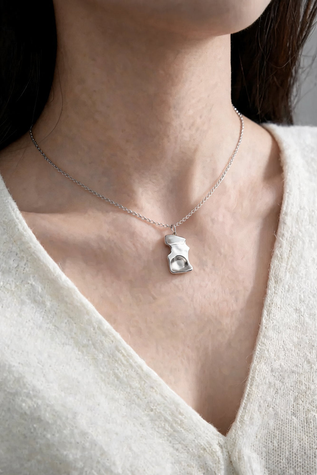 The Molten Pendant in silver, worn with an ivory knit